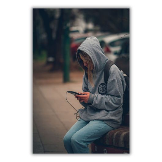 A teenager in a hooded sweatshirt, alone, looking down at a phone