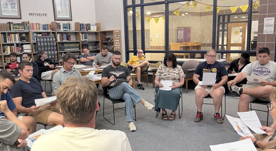 Teachers seated in a circle in a school library, each holding a handout, during a Teach Different workshop